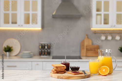 Breakfast served in kitchen. Crunchy toasts, jam and orange fresh on white table. Space for text