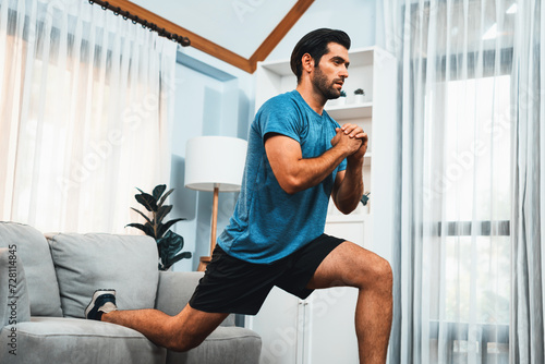 Athletic and sporty man doing squat during home body workout exercise session for fit physique and healthy sport lifestyle at home. Gaiety home exercise workout training concept.