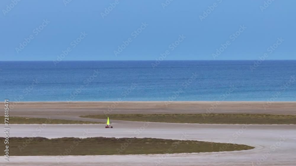 Aerial shot of a person piloting a land yacht across the smooth sands of an undisturbed beach, with the colorful sail billowing in the sea breeze Aerial shot of a person piloting a land yacht across the smooth sands of an undisturbed beach, with the colorful sail billowing in the sea breeze