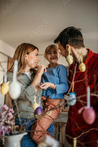 Family of three immersed in the artistic process of painting eggs and embellishing their Easter tree in the dining room