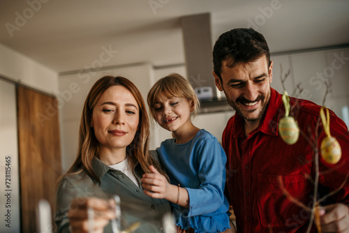 Parents and child creating a festive atmosphere at their dining table  painting eggs and hanging decorations on their Easter tree