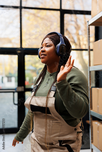 Cheerful manager wearing headphones listening music during work break in storehouse, dancing and having fun. African american employee with industrial overall doing merchandise quality control © DC Studio