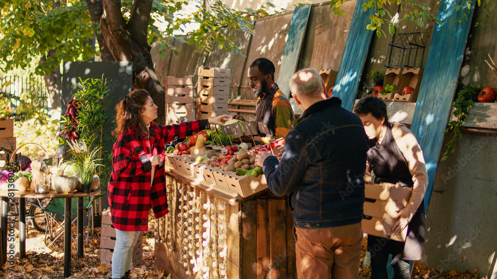 Obraz premium Young farmer serving client with various produce and selling homegrown farm veggies at local food market. Female customer buying fresh organic fruits and vegetables, farming nutrition.