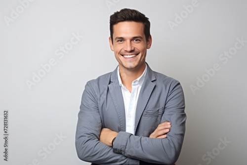Portrait of a smiling young businessman with arms crossed against grey background