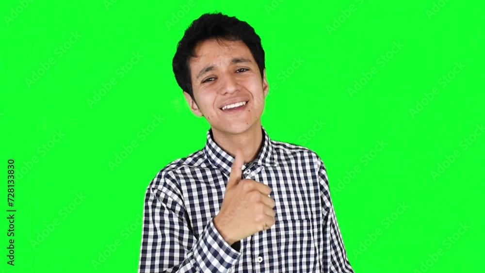 Joven hombre caucasico con camisa a cuadros sonríe y hace gesto de aprobación o like con su pulgar arriba sobre un fondo verde