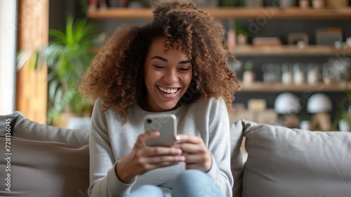 Happy relaxed young woman sitting on couch using cell phone, smiling lady laughing holding smartphone, looking at cellphone enjoying doing online ecommerce shopping in mobile apps or watchin photo