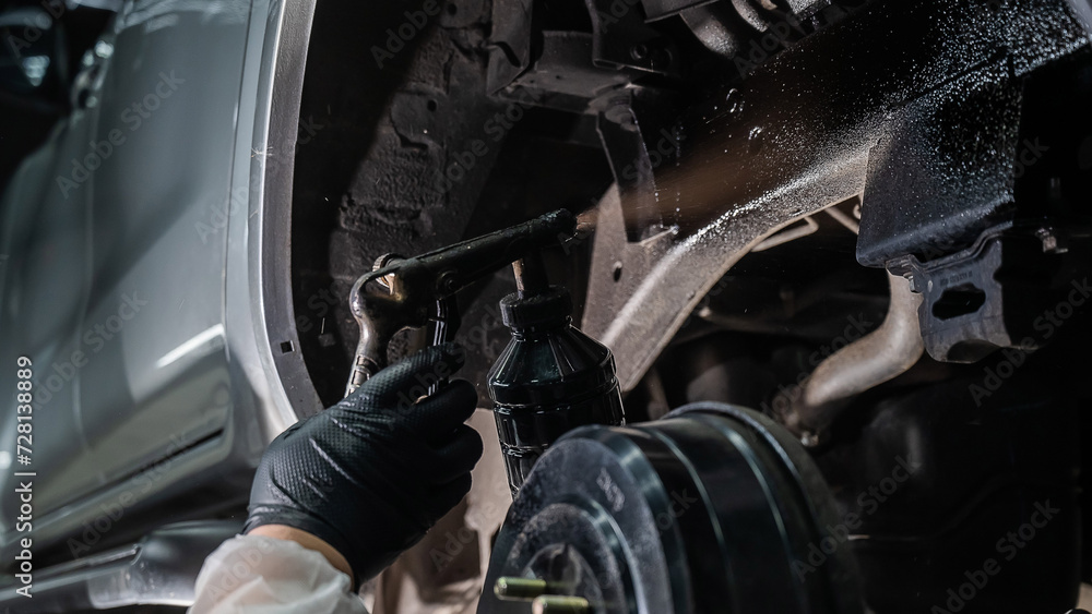 The master sprays an anti-corrosion compound on the bottom of the car.