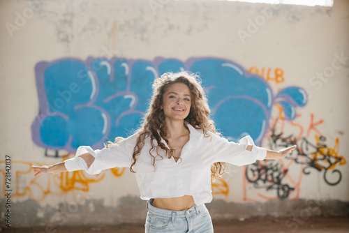 Stylish young woman with curly hair posing against the background of a graffiti wall.