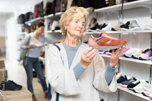 Mature european woman who came to a shoe store for shopping, chooses sports sneakers, standing near the shelves with the goods photo