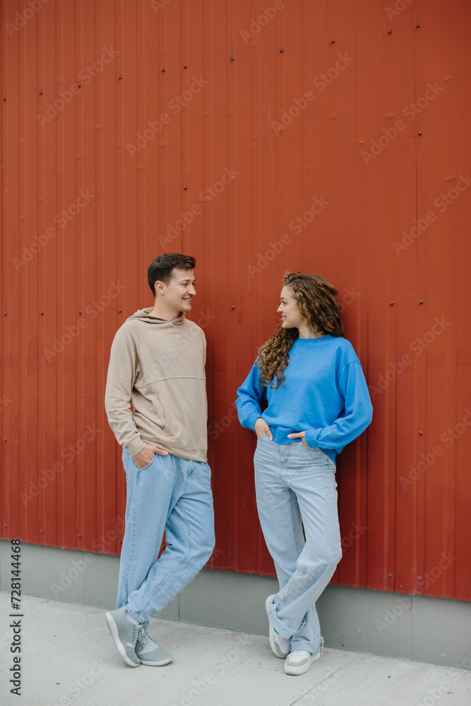 A couple of friends, a boy and a girl, are talking on the background of a red wall outdoors. A couple of friends, a boy and a girl, are talking on the background of a red wall outdoors.