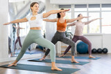 Young girl with group of active people doing stretching exercises during yoga class in sports club
