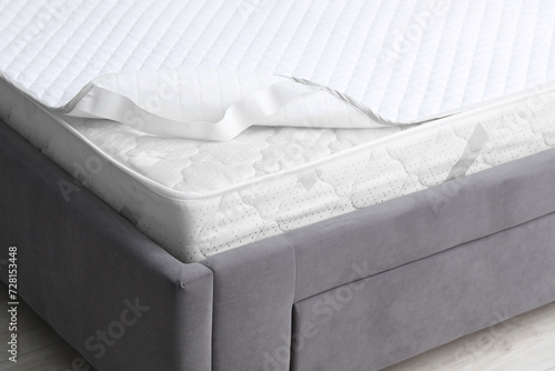 New soft mattress with protector on grey bed indoors, closeup photo