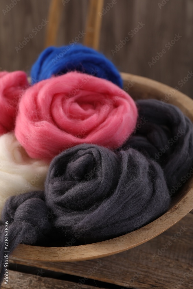 Fototapeta premium Colorful felting wool in bowl on wooden table, closeup