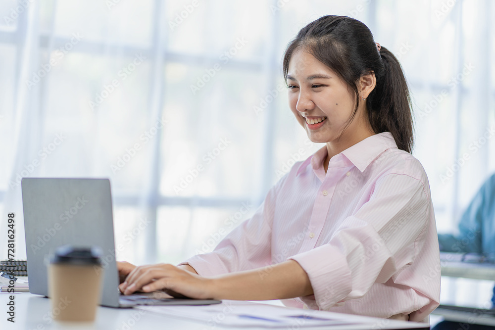 Cheerful Asian woman working with laptop in office, happy in formal suit working in office Charming smiling female office worker, financial accounting concept Cheerful Asian woman working with laptop in office, happy in formal suit working in office Charming smiling female office worker, financial accounting concept