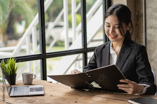 Cheerful Asian woman working with laptop in office, happy in formal suit working in office Charming smiling female office worker, financial accounting concept photo