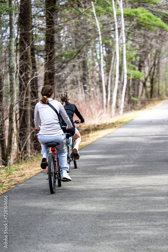 Two young slender girls ride bicycles along an asphalt path in a forest belt taking care of their figure © vit