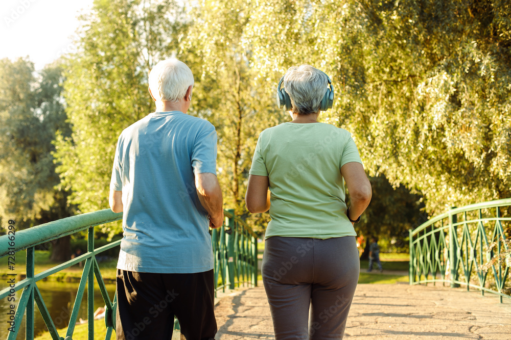 Obraz premium Senior mature couple running together in the park looking at each other while jogging slimming exercises.