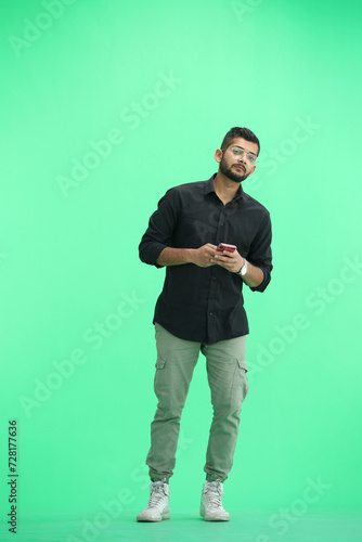 A man, on a green background, in full height, with a phone © Katsiaryna