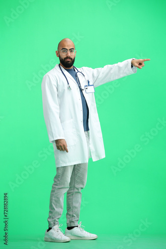 The male doctor, on a green background, in full height, points to the side