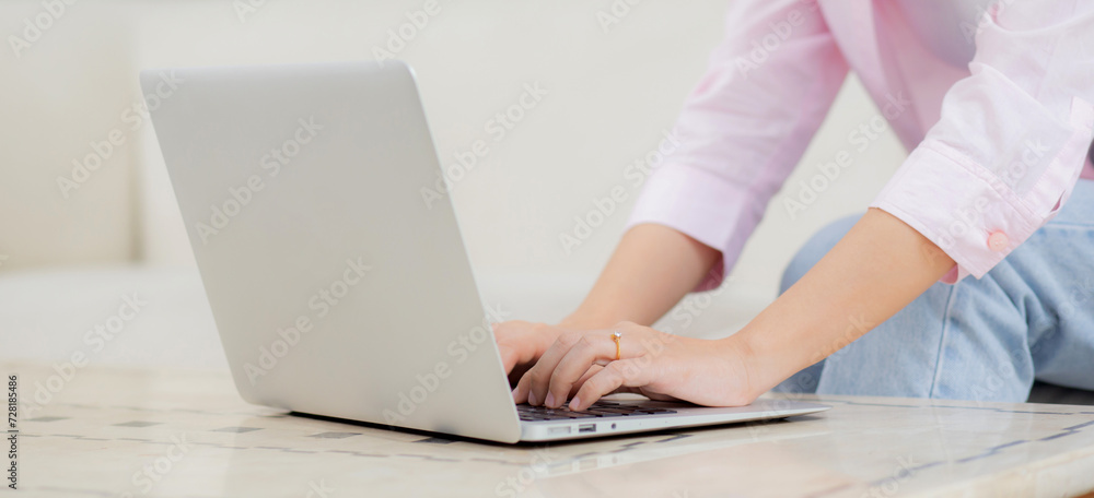 Fototapeta premium Young asian business woman work from home with laptop computer online to internet on sofa in living room, freelance is female using notebook sitting on couch with comfort and relax, lifestyle concept.
