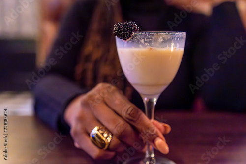 An elegant hand cradles a sophisticated cocktail, garnished with a plump blackberry. The creamy beverage swirls enticingly in the glass, promising indulgence and relaxation. Perfect for upscale bars, 