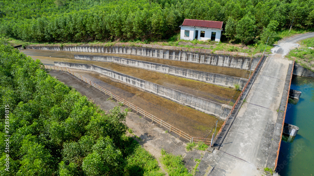 Aerial view of an empty dam, multi-tiered aquaculture farm with a small building, surrounded by lush greenery, highlighting sustainable fishing practices