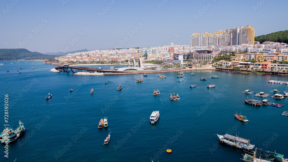 Aerial view of a coastal cityscape with modern architecture, a large bridge, and boats in the harbor on a sunny day, with no specific holiday depicted