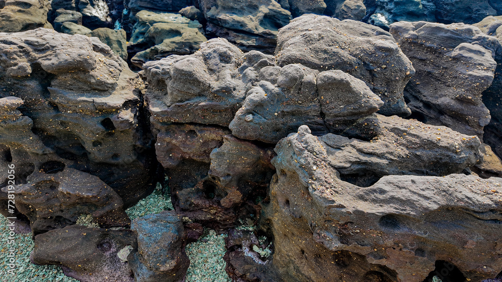 Rugged, weathered volcanic rocks with holes and crevices near a coastline, depicting natural geological textures and formations Rugged, weathered volcanic rocks with holes and crevices near a coastline, depicting natural geological textures and formations