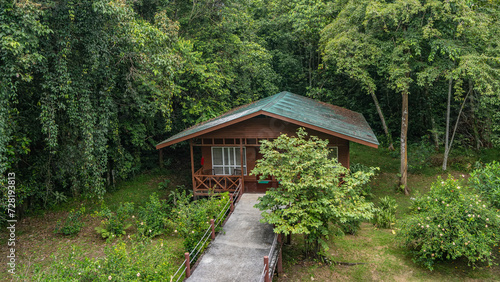 A lodge in the Borneo rain forest. A concrete footpath with rope railings leads to a wooden one-story house. Lush thickets of green tropical vegetation around. Malaysia. Sandakan.  
