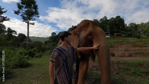 White man in northern Thai shirt walks up and pets elephant appreciating the natural beauty