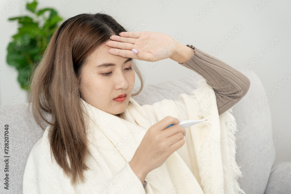 Young Asian woman having high fever while checking body temperature, female sneezing and runny nose with seasonal influenza, allergic, digital thermometer, virus, coronavirus, illness, respiratory. Young Asian woman having high fever while checking body temperature, female sneezing and runny nose with seasonal influenza, allergic, digital thermometer, virus, coronavirus, illness, respiratory.