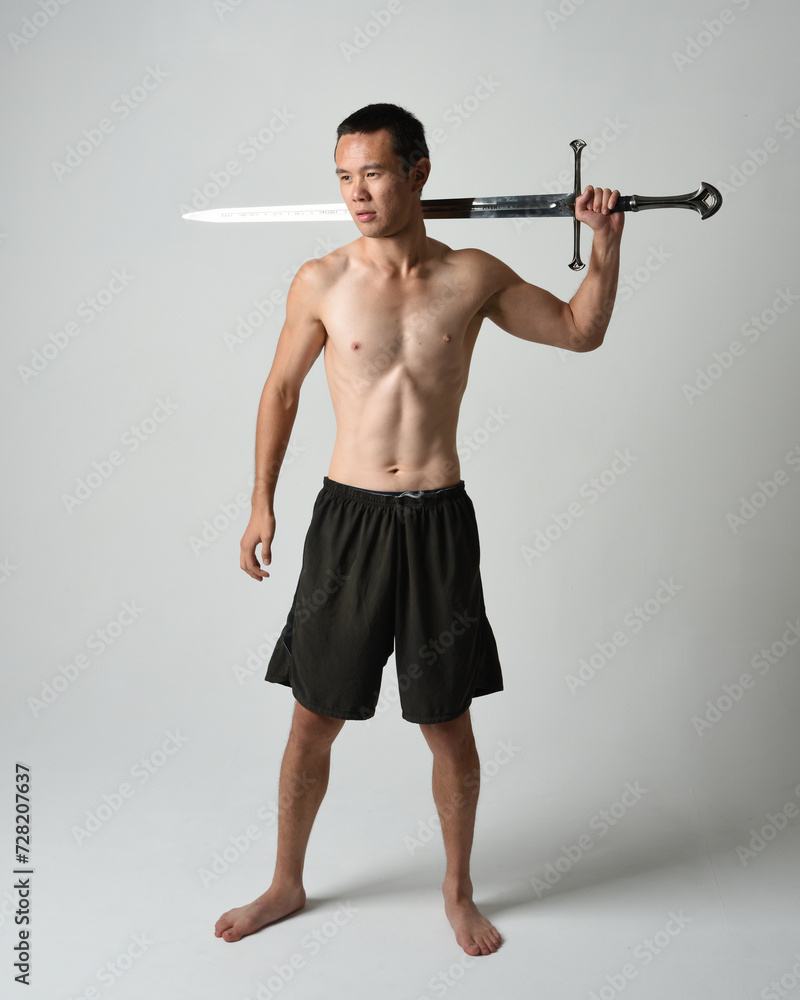 Full length portrait of fit handsome asian male model, wearing gym shorts and shirtless. Holding sword weapons whilst in warrior training action poses, isolated on white studio background. Full length portrait of fit handsome asian male model, wearing gym shorts and shirtless. Holding sword weapons whilst in warrior training action poses, isolated on white studio background.