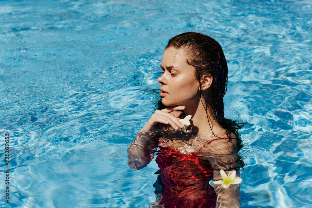 Young woman in swimming pool in red swimsuit with beautiful smile and Balinese flower in the sun swimming in the pool, concept of relaxation on vacation.