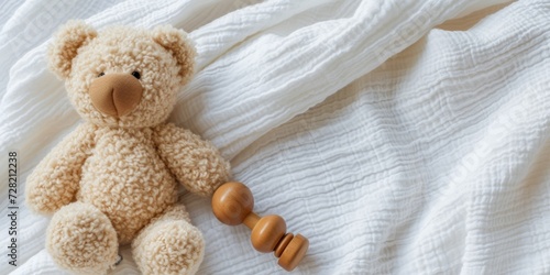 Teddy bear and natural wooden rattle toy on white blanket throw background. Top view, copyspace