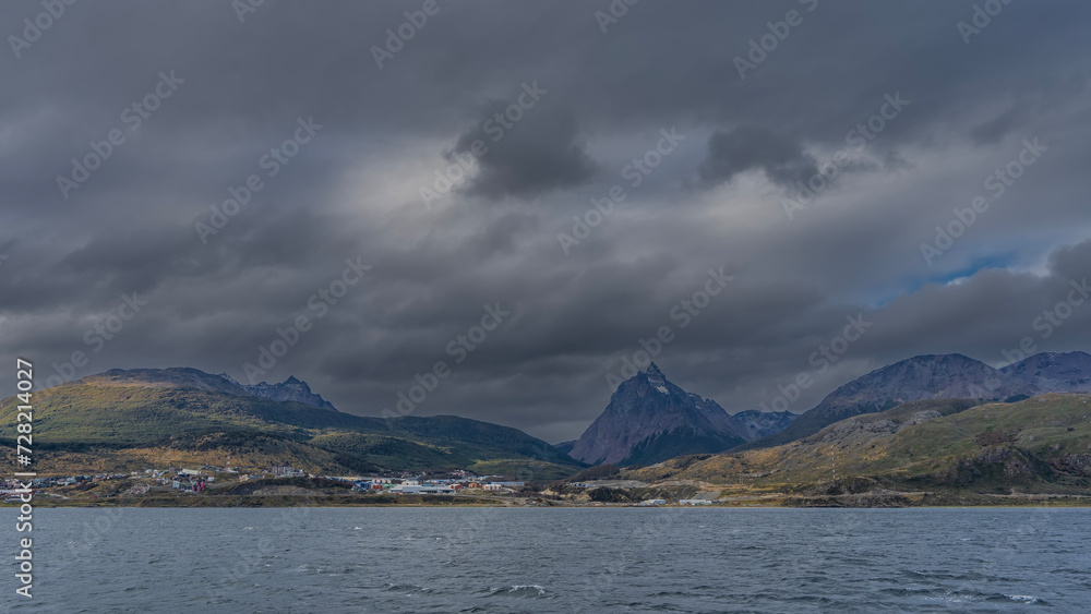 The beautiful landscape of Patagonia. View from the Beagle Canal. The Andes mountain range against a cloudy sky. The townhouses of Ushuaia are near the shore in the valley. Argentina.