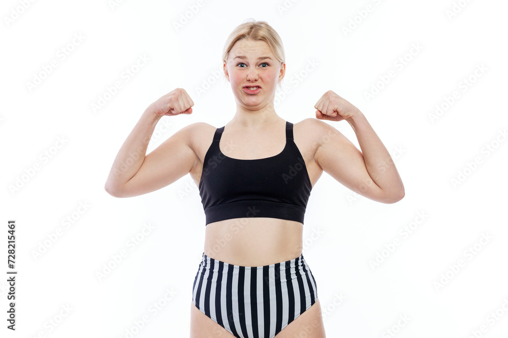 A young teenage girl in a sports swimsuit shows her biceps. A funny blonde with freckles in a black top and striped panties makes faces. White background. A young teenage girl in a sports swimsuit shows her biceps. A funny blonde with freckles in a black top and striped panties makes faces. White background.