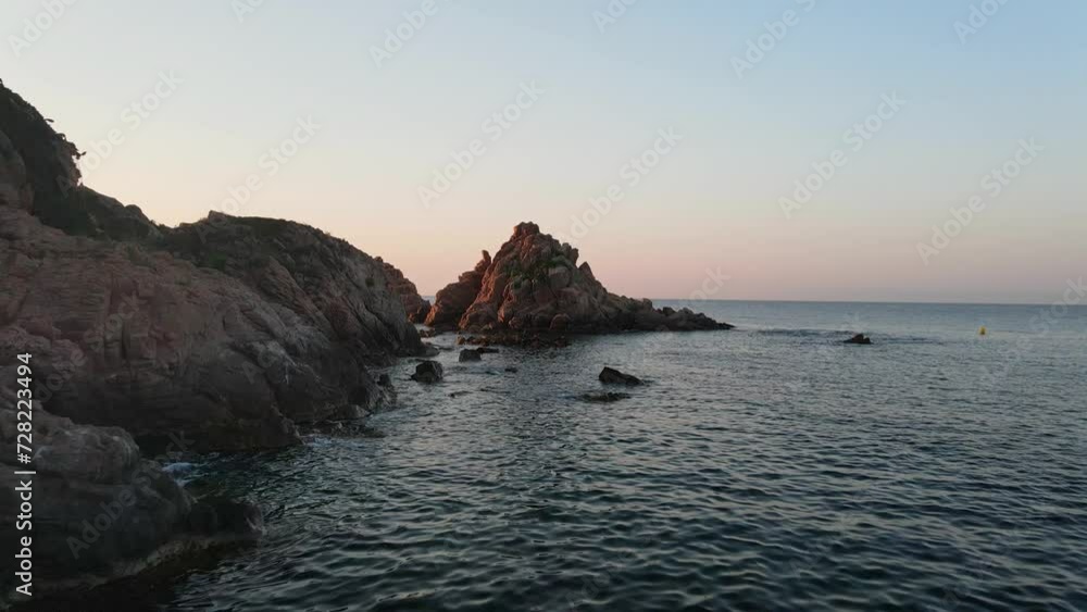 Dusk view of Costa de Blanes with serene sea, rocky shores and a small boat cruising Dusk view of Costa de Blanes with serene sea, rocky shores and a small boat cruising
