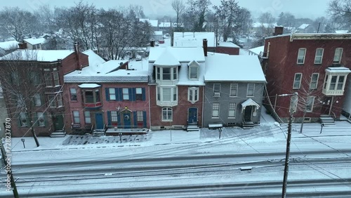 Row houses with snowy roofs on a winter day, streets lined with fresh snow tracks. Aerial.