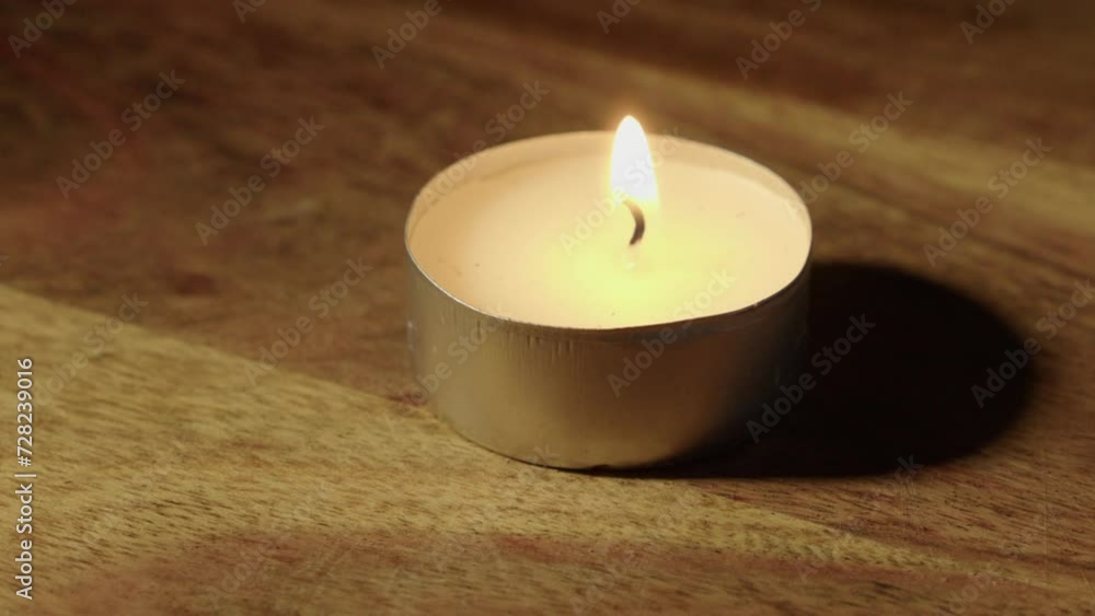 Closeup: One tea candle on wooden countertop is lit with burning match Closeup: One tea candle on wooden countertop is lit with burning match