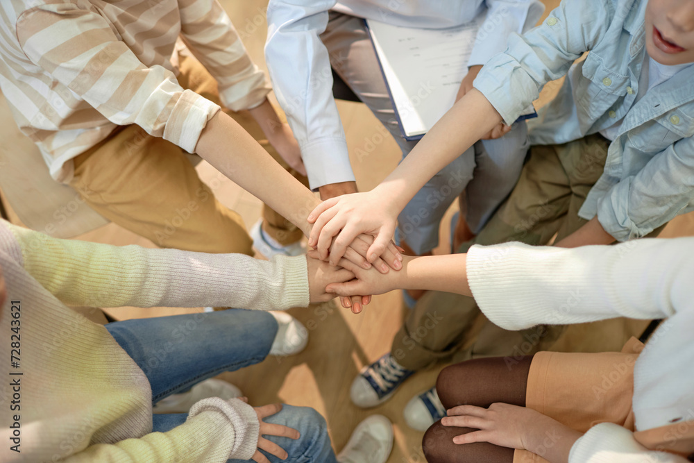 Top view closeup of children stacking hands and huddling celebrating success and teamwork in schoolwith copy space