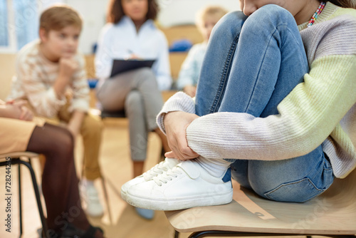 Close up of depressed young girl hugging knees and sharing mental health problem during support group for childrenwith copy space photo