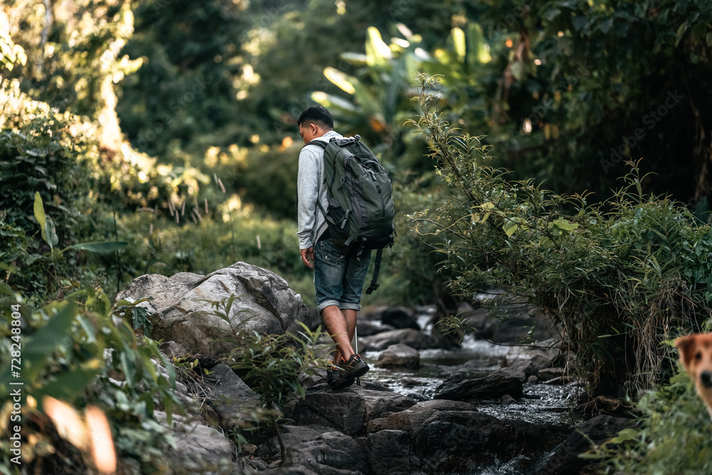 Hikers walk on rocks in the stream flowing from the waterfall in the forest. Hikers walk on rocks in the stream flowing from the waterfall in the forest.