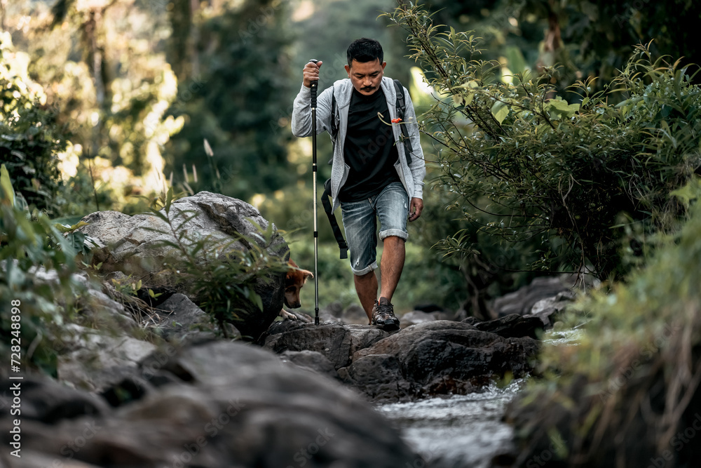 Hikers walk on rocks in the stream flowing from the waterfall in the forest. Hikers walk on rocks in the stream flowing from the waterfall in the forest.
