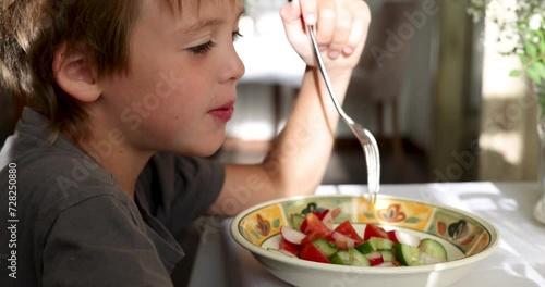 Hungry boy eats vegetable salad sitting at table in grandmother country house. Calm atmosphere in apartment in sunny weather. Satisfying hunger