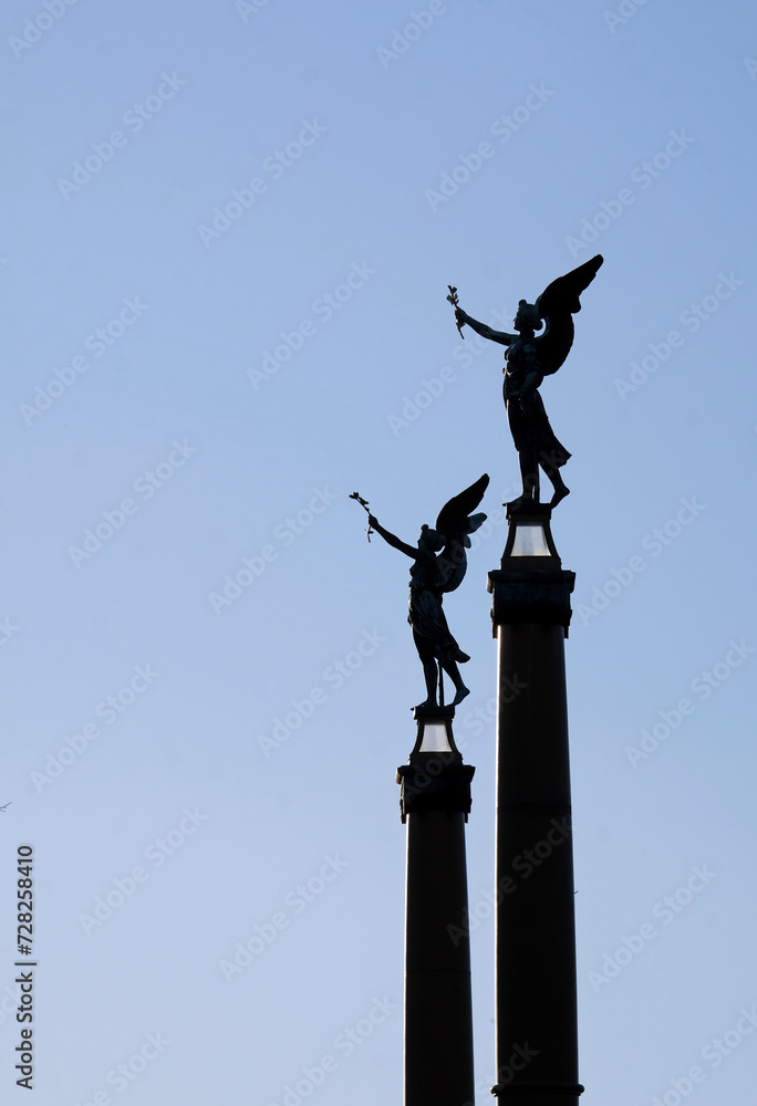 Two angel statues with wings against the blue evening sky Two angel statues with wings against the blue evening sky