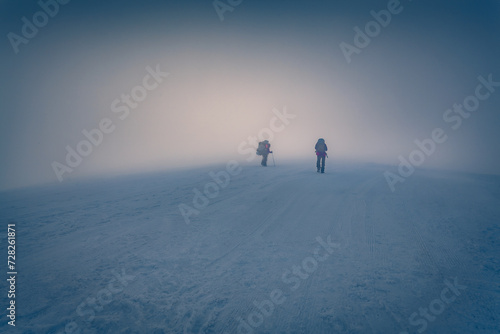 Two tourists climbing to the top of summit. Foggy winter scene of Carpathian mountains, Ukraine, Europe. Fantastic sunrise on ski resort Dragobrat. Traveling concept background..