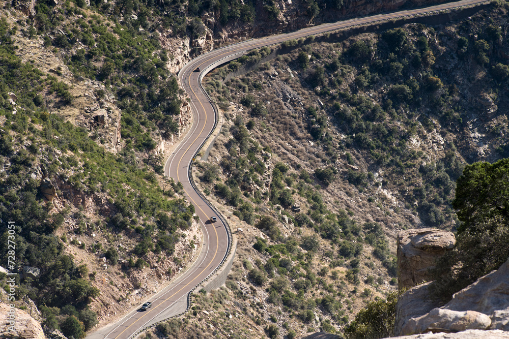 Looking down at winding mountain road in daylight with cars on it