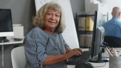 Medium portrait of cheerful Caucasian mature woman sitting in front of computer attending group class, looking at camera photo