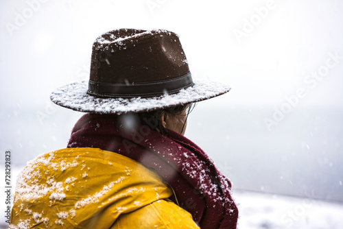 Solo  traveler with yellow rain coat and cowbow hat lookng away under snow, back shot photo