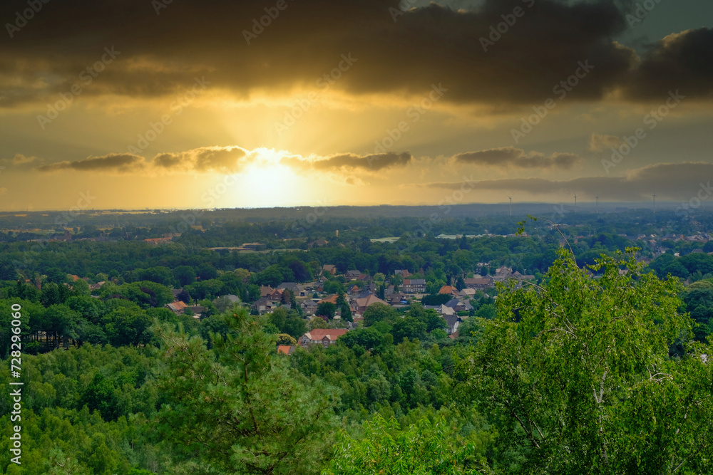 This evocative image captures the dramatic beauty of a suburban landscape bathed in the golden light of a setting sun. The heavy cloud cover adds a dramatic contrast to the sun's bright rays piercing